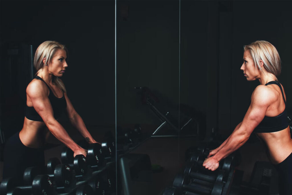 blond girl at gym in front of the mirror with dumbells